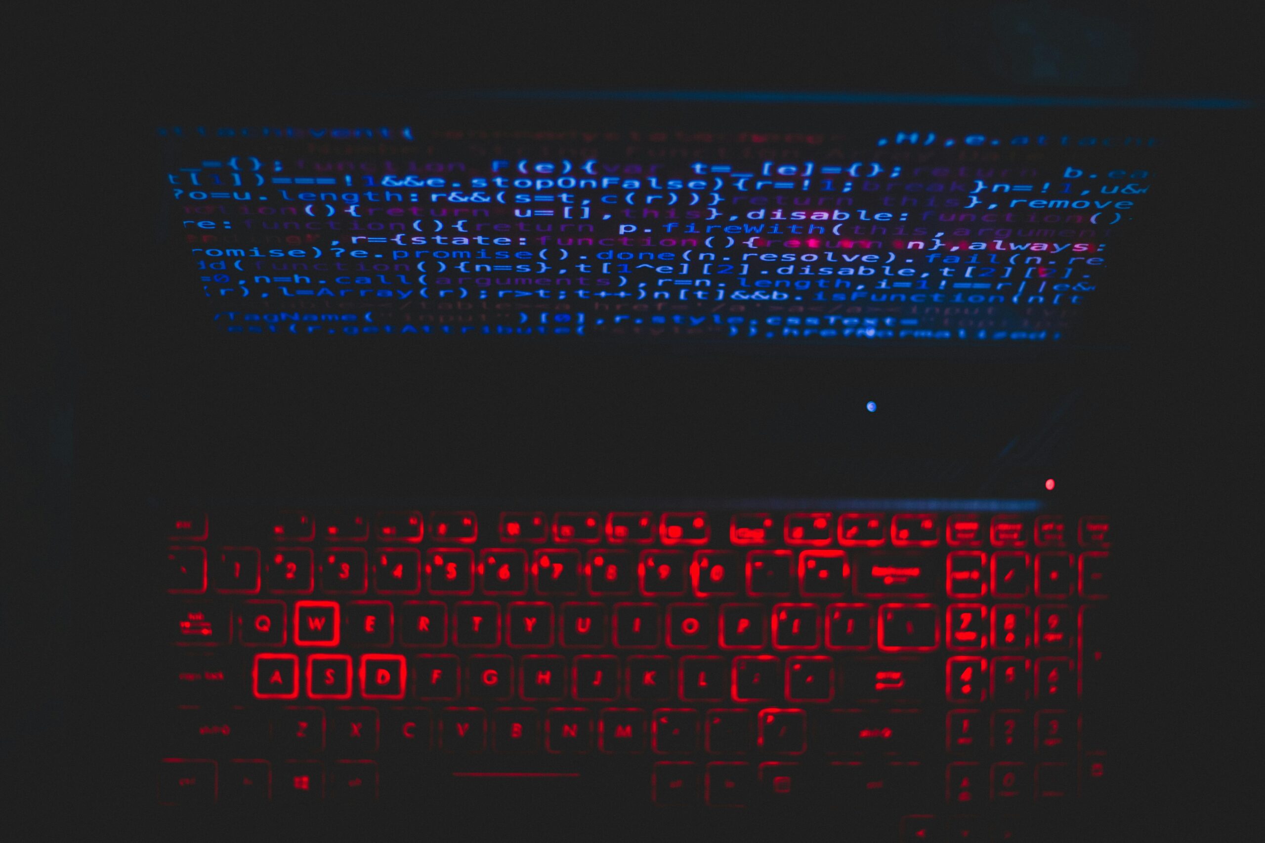 Dark-themed laptop setup with a red glowing keyboard and code on screen, ideal for tech enthusiasts.