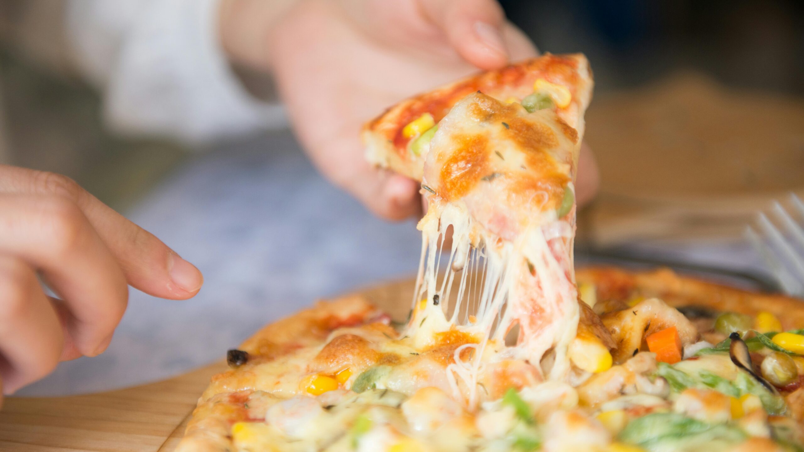 Appetizing close-up of a cheesy pizza slice with toppings, being pulled from a freshly baked pie.