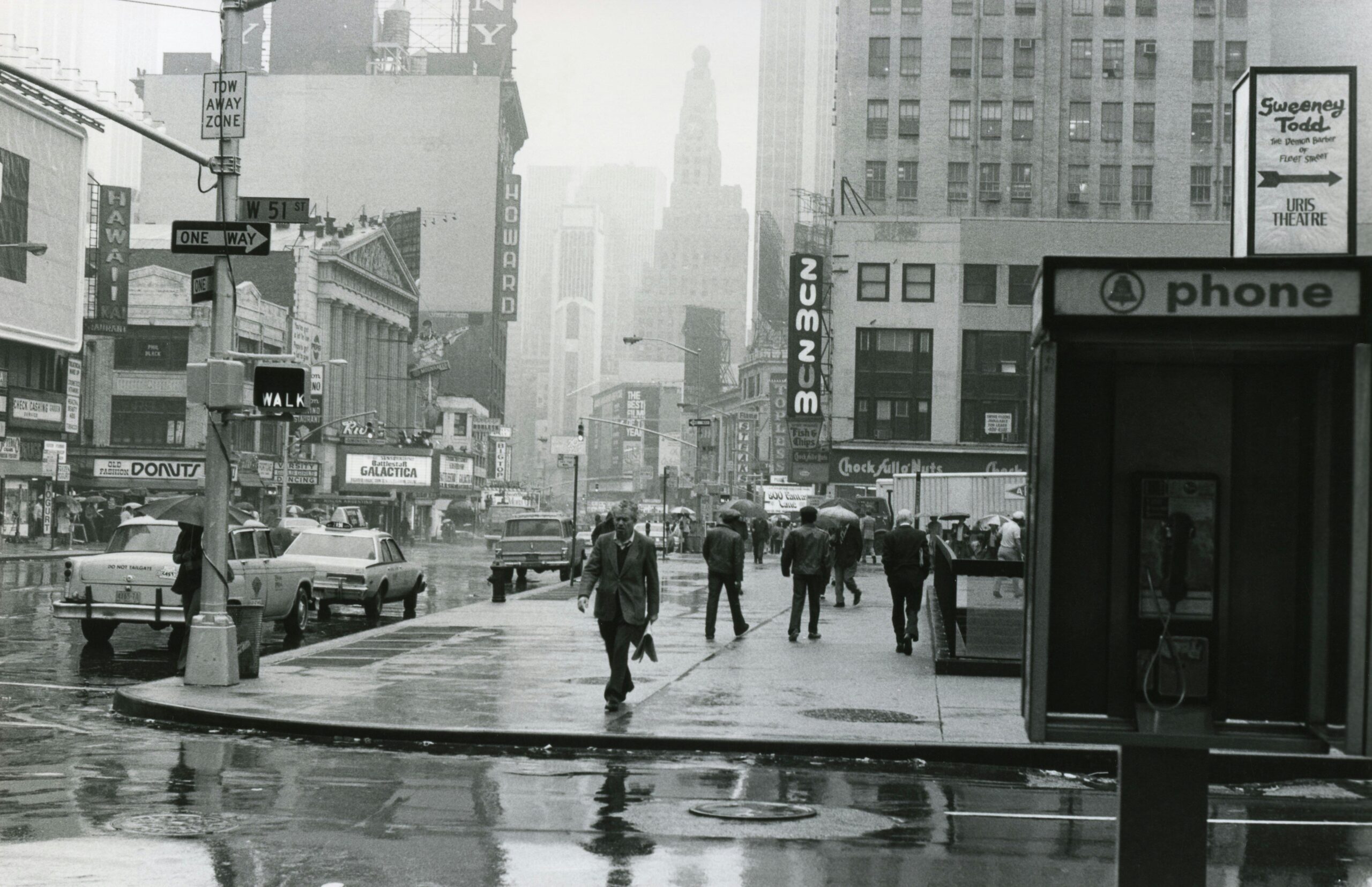 Vintage cityscape of New York with people and cars on a rainy street.