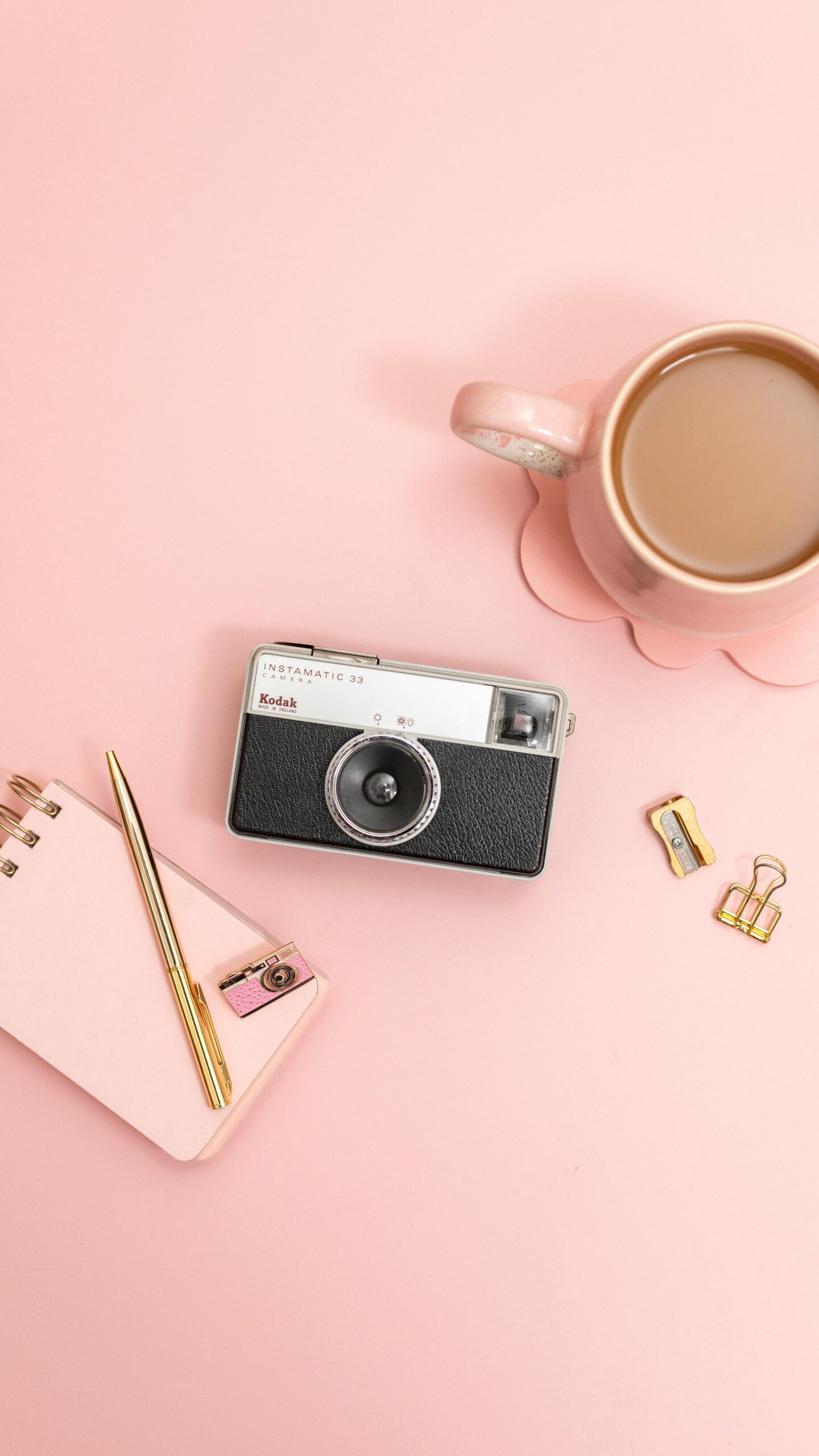 Stylish pink desk flat lay with vintage camera, coffee mug, and stationery.