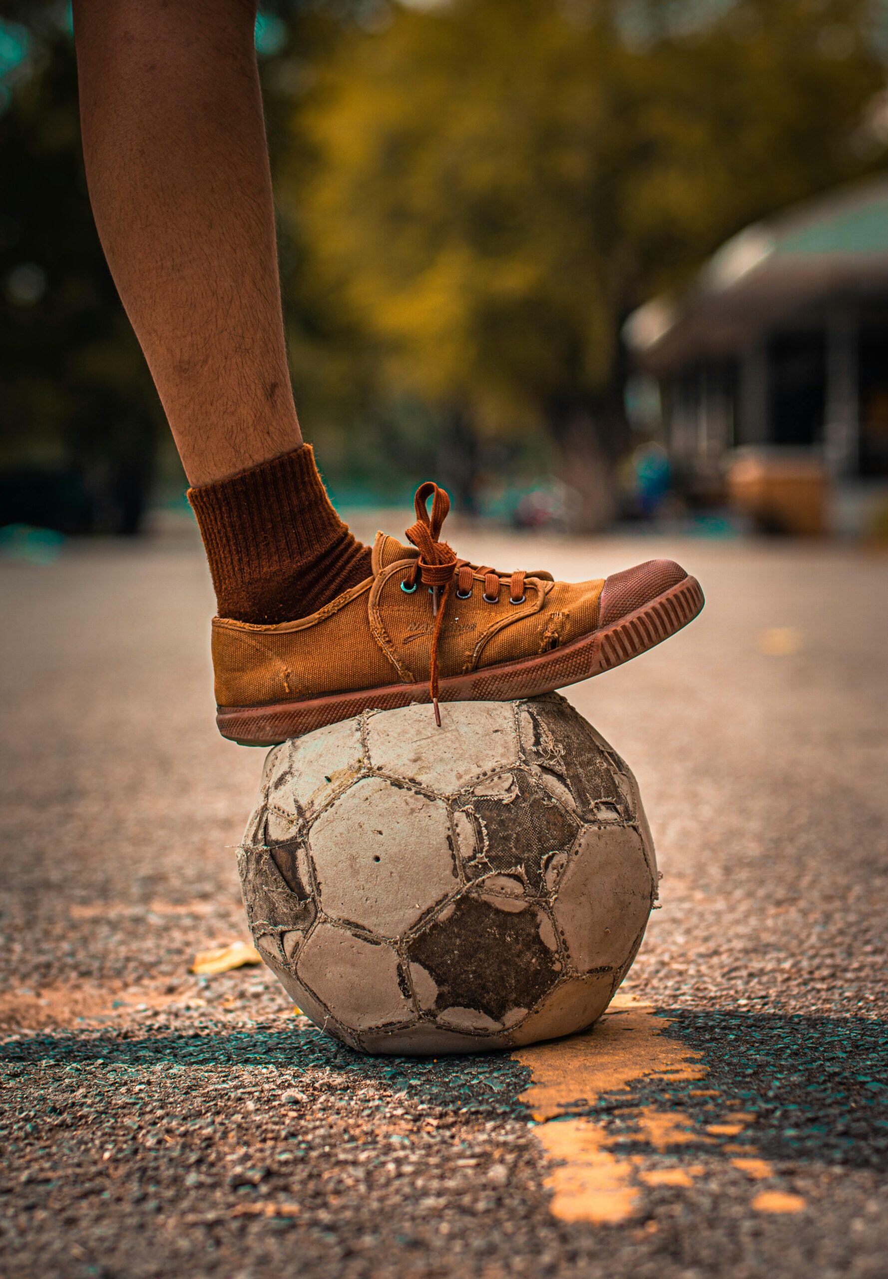 An aged soccer ball under a foot in casual footwear on an outdoor surface.