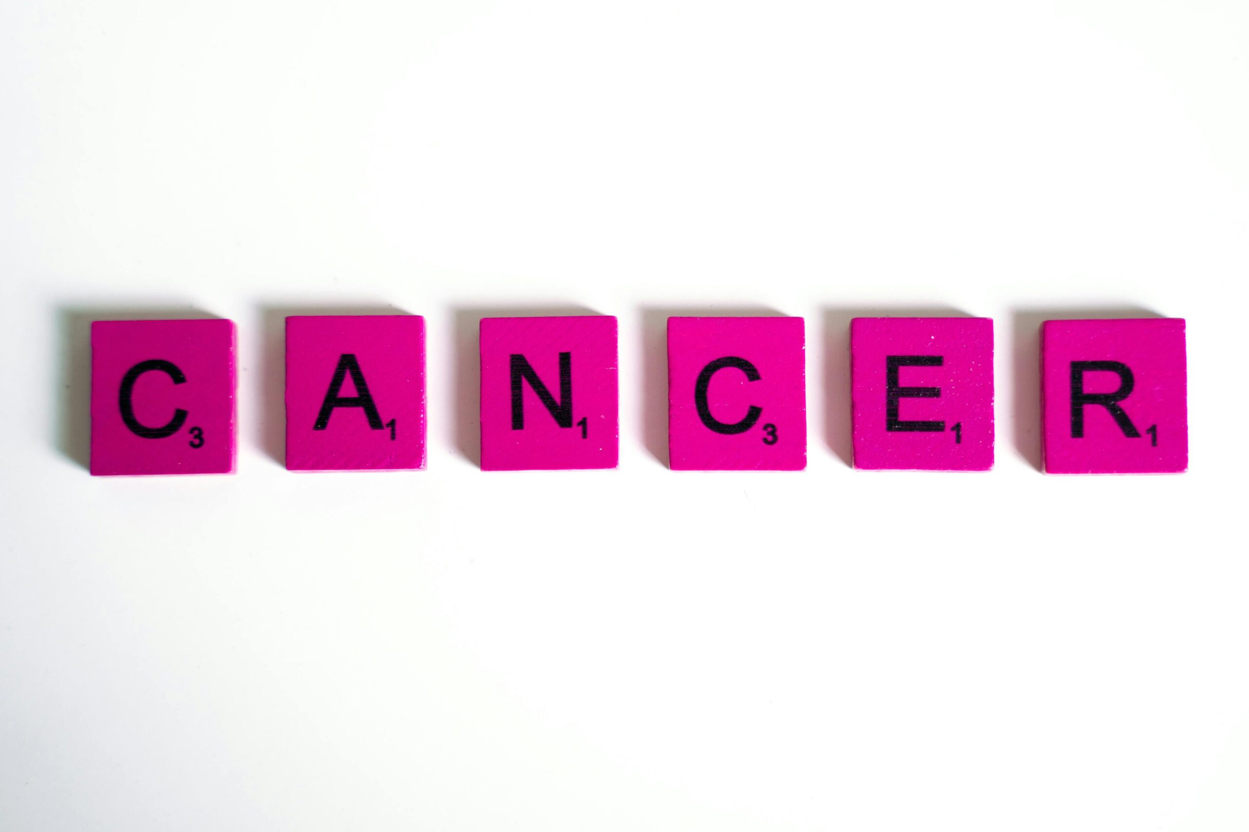 Word 'cancer' spelled with pink letter tiles on a white background symbolizing awareness.