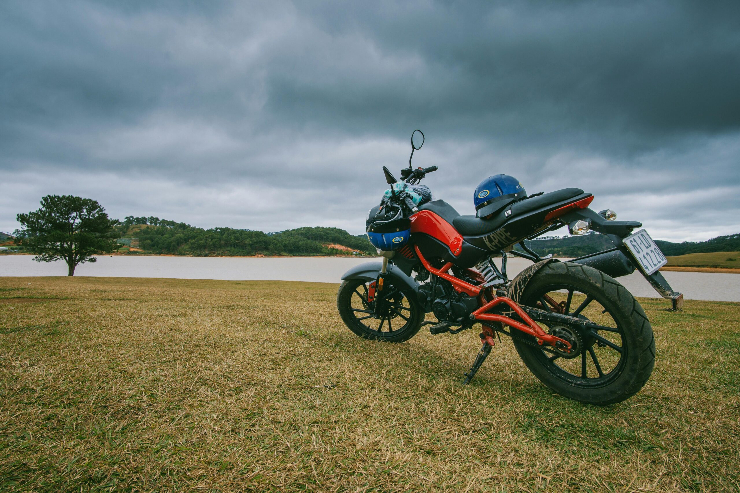 A scenic view of a parked motorcycle near a calm lake under stormy clouds, capturing the essence of adventure and nature.