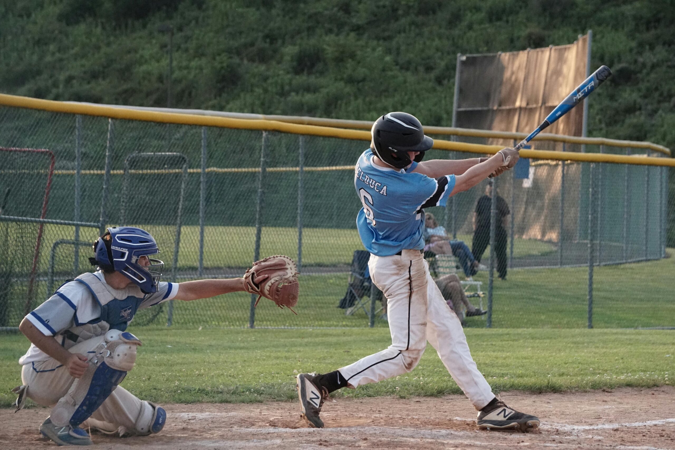 Youth baseball player swings the bat during a game on a sunny day.