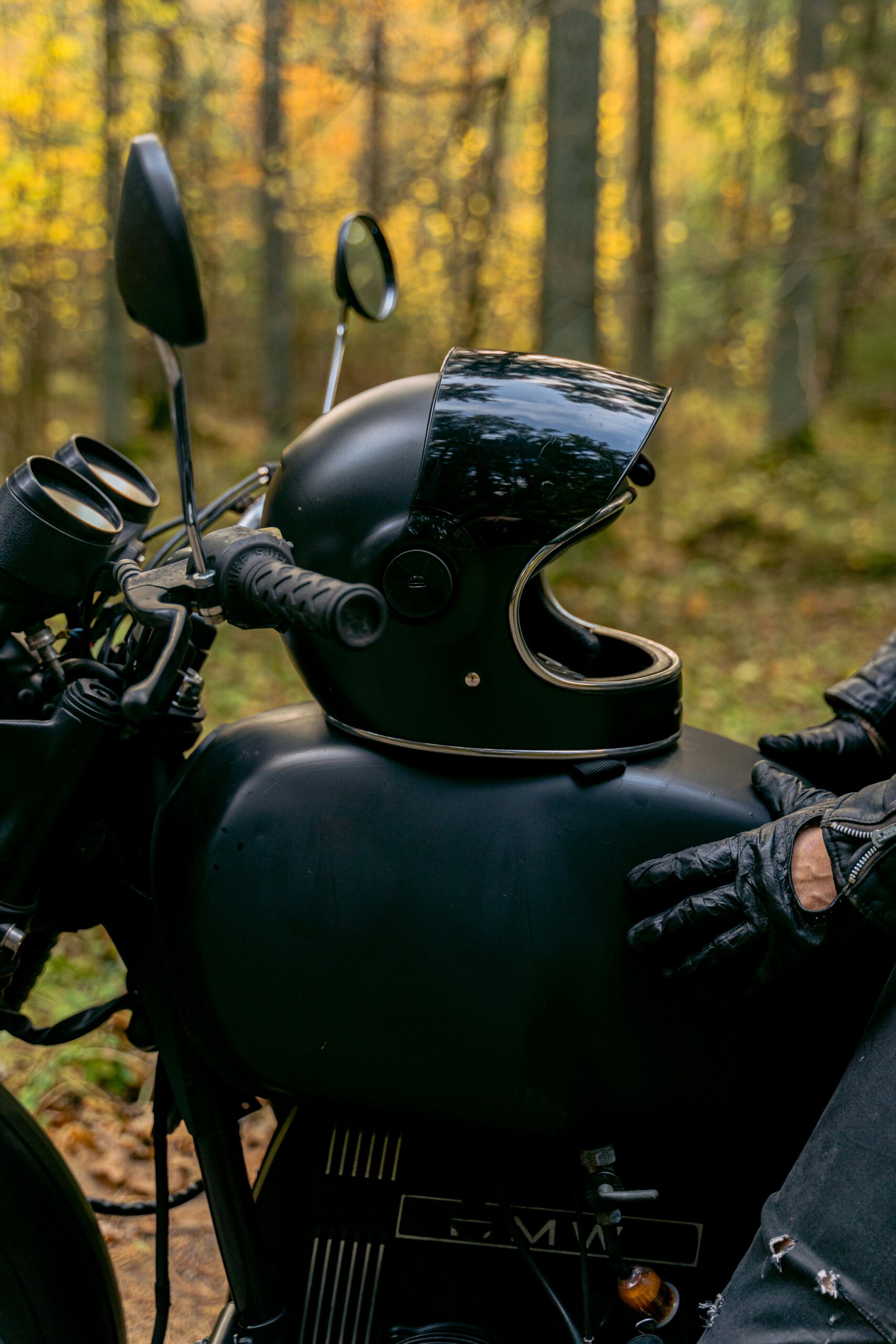 Close-up of a black motorcycle with helmet in an autumn forest setting, showcasing adventure themes.